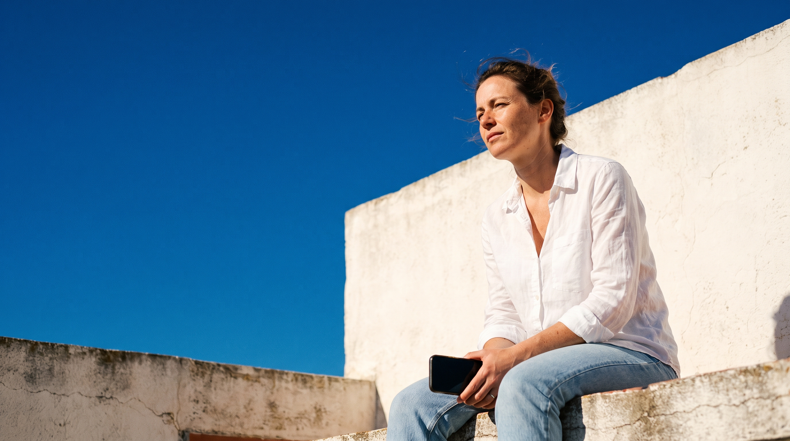 A woman sitting on a sunlit rooftop, looking calmly into the distance
