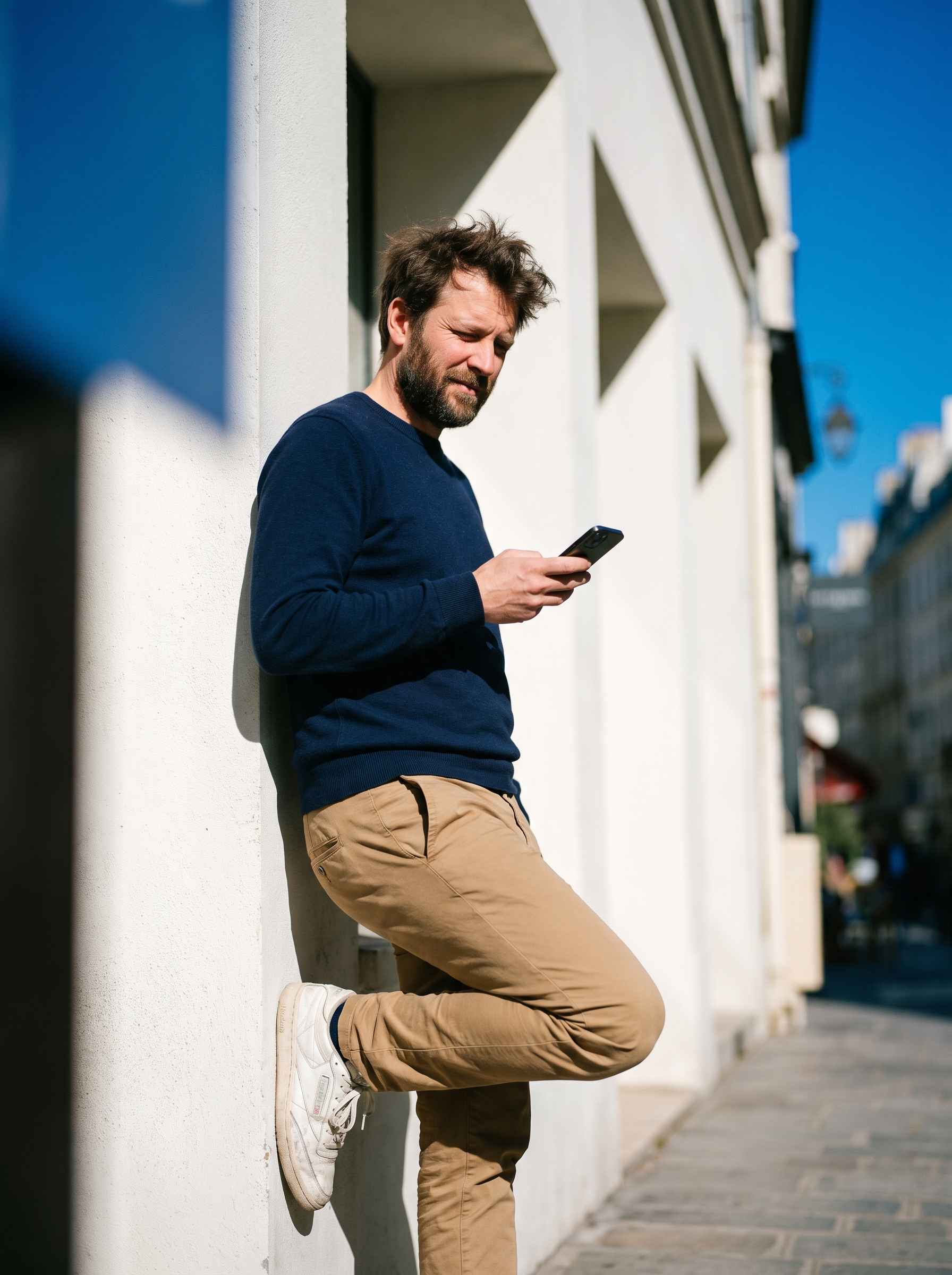 A man reading on his phone against a bright sunlit wall